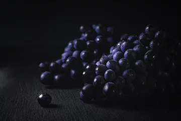Fotobehang A bunch of dark grapes on a black background horizontal with copy space © Miroslava