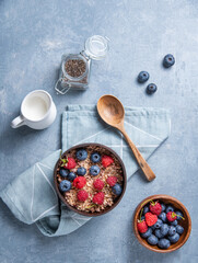 energy muesli with raspberry,  blueberry, chia seeds and  milk into coconut bowl on blue background