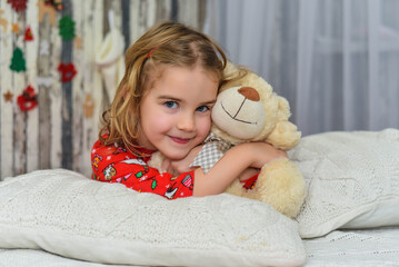 Beautiful little girl holding teddy bear, in the bright New Year's interior