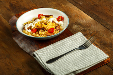 Pasta with chicken, tomatoes and cheese in a gray plate on a stand on a napkin with a fork.