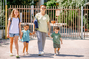 Happy school children going to school with grandmother. Pupils and grandma with a backpack go to kindergarten and school. Togetherness happy moments.