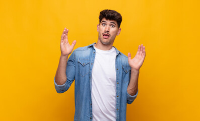 young handsome man looking shocked and astonished, with jaw dropped in surprise when realizing...