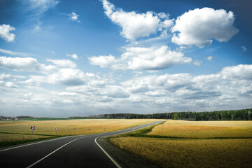 Road between yellow fields. Landscape with blue skue and big clouds.