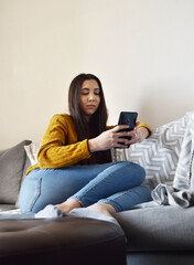Girl with her smartphone sitting on the couch watching the social networks