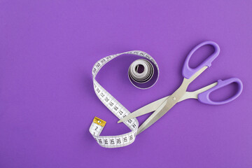 Closeup on white centimeter and scissors on the violet  background