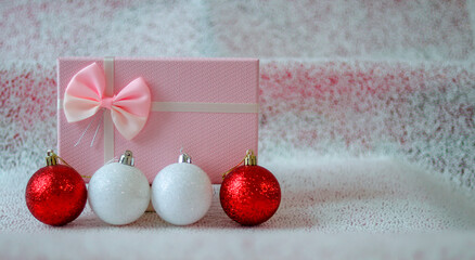 Gift box of soft pink color and Christmas balls of red and silver color on a light background that imitates snow. Free space. Christmas background, holiday card.