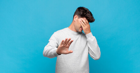 young handsome man covering face with hand and putting other hand up front to stop camera, refusing...