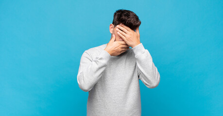 young handsome man covering face with both hands saying no to the camera! refusing pictures or...
