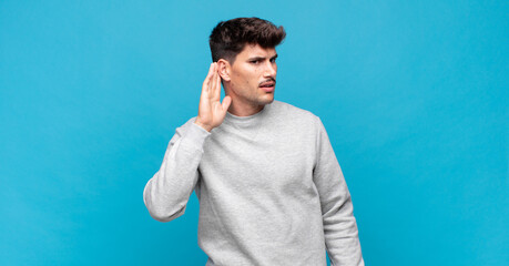 young handsome man looking serious and curious, listening, trying to hear a secret conversation or...