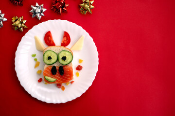 Funny sandwich with edible symbol of 2021 bull cow made from toast bread, red fish, cucumber, tomato, cheese and raisins. Breakfast idea for kids. christmas food top view , food art.