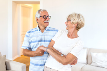 Happy mature loving couple dancing in living room relaxing at home on weekend together, smiling...