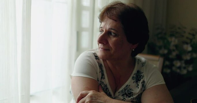 Pensive older senior woman sitting at home by window