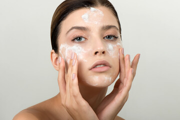 Beautiful young girl cleansing face with cosmetic facial skincare foam, gel or soap.
