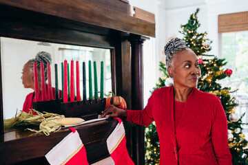 Senior Black woman setting up the Kwanzaa holiday setting and kinara with Christmas tree in background
