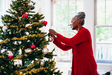 Senior Black woman decorating the Christmas tree with ornaments