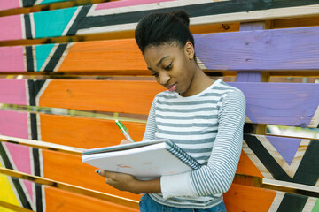 Young Black teen girl drawing in notebook outside at school