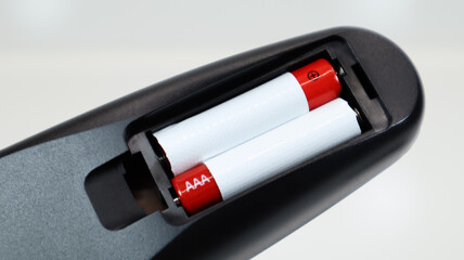 Black TV remote control with AAA alkaline batteries in red and white on a white background. Battery...