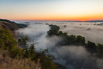 Beautiful panoramic landscape with river valley covered by thick fog in autumn in the early morning. Sunrise.