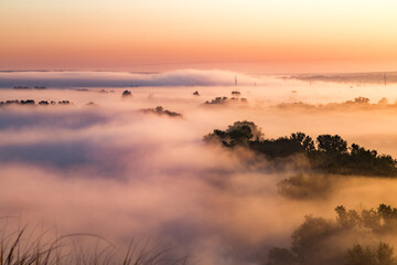 Beautiful panoramic landscape with river valley covered by thick fog in autumn in the early morning. Sunrise.