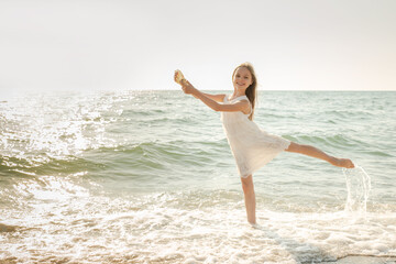 Fototapeta na wymiar Portrait of beautiful little girl is playing with seashell in sea waves.
