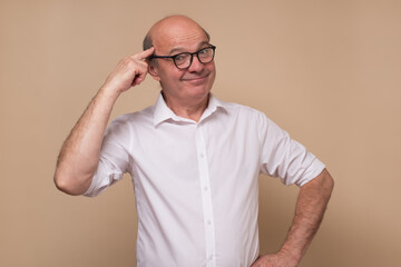 Mature european man with beard holds fingers on temple having idea. Studio shot.