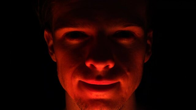 A scary and evil criminal man with a crazy smile and a creepy look of violence out of the dark night.