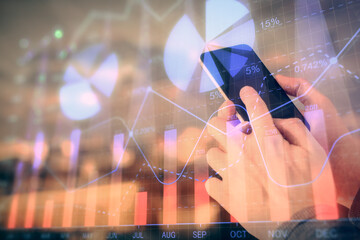 Double exposure of man's hands holding and using a digital device and forex graph drawing. Financial market concept.