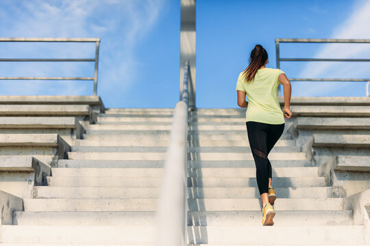 Back view of slim woman in sportswear running on stairs