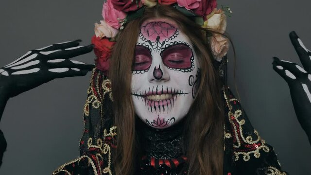a woman in the image of death (Santa Muerte or sugar Mexican skull) poses for the camera, covering and revealing her face with her hands. halloween makeup, close-up