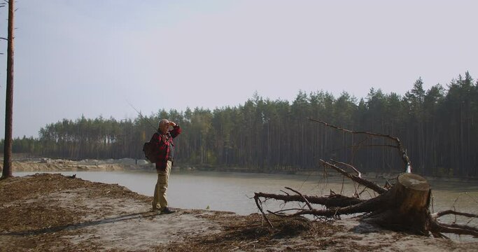 fisherman is looking around on forest lake, admiring nature in autumn season, fishing place and relax