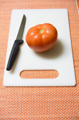 Tomate rojo  y cuchillo sobre tabla de cortar de color blanco 