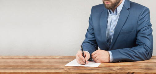 A man businessman is sitting at a wooden table. The hand writes on a blank sheet.