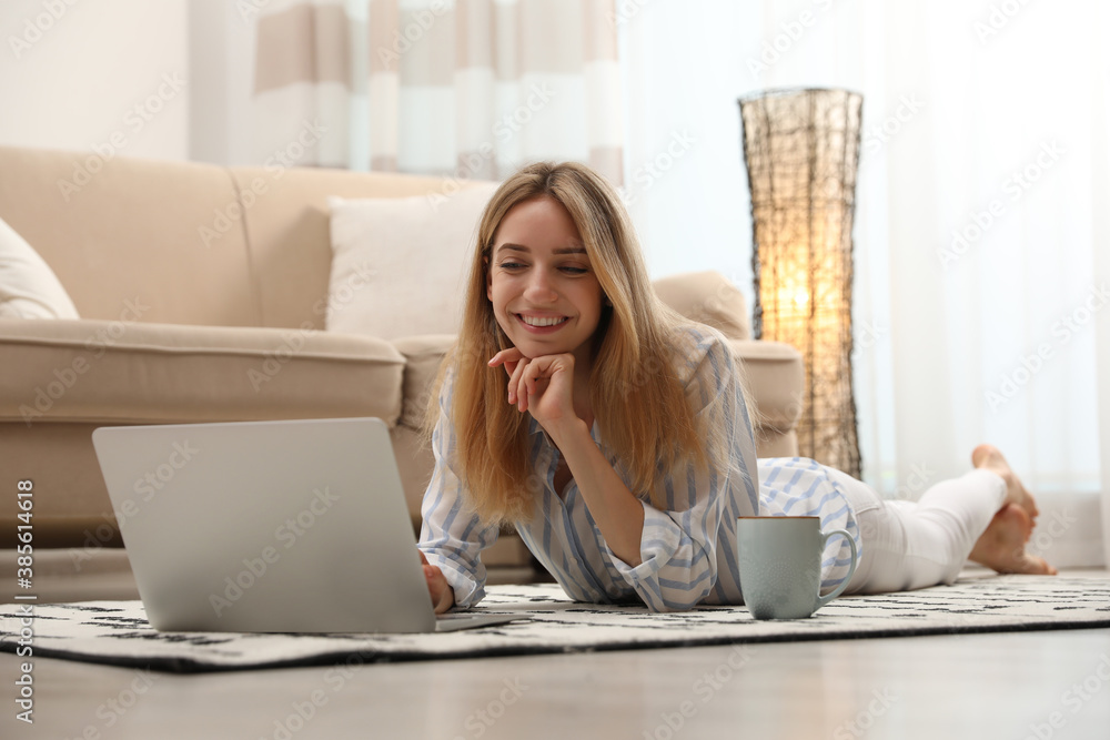 Wall mural Pretty young woman with laptop lying on floor at home