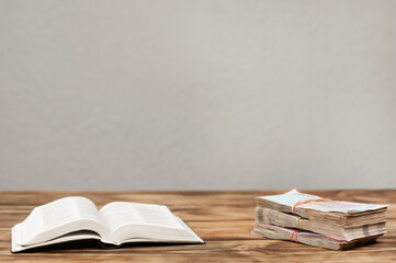 Open Bible book on the table. Stack of money. Priority concept