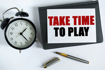On the table there is a clock, a pen, a notebook and a card on which the text is written - TAKE TIME TO PLAY