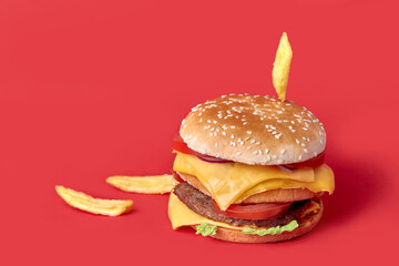 A large juicy double Burger falls on top of the fries. Burger with cheese, vegetables and two cutlets. Red background.