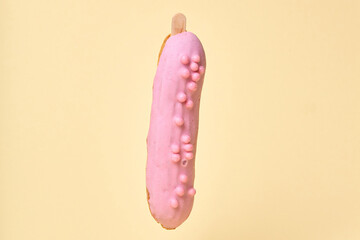 Vertically arranged Eclair in chocolate pink glaze. Covered with colored dragees. Yellow isolated background.