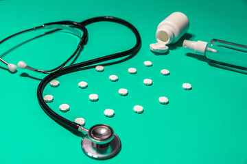 Poukładane tabletki leków na zielonym tle wyciągnięte z pudełka, kapsułki, płyn w aerozolu oraz stetoskop