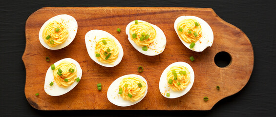 Homemade Deviled Eggs with Chives on a rustic wooden board on a black surface, top view. Flat lay, overhead, from above.