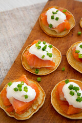 Homemade Blini with Smoked Salmon, Creme and Chives on a rustic wooden board, side view. Copy space.