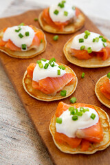 Homemade Blini with Smoked Salmon, Creme and Chives on a rustic wooden board, low angle view.