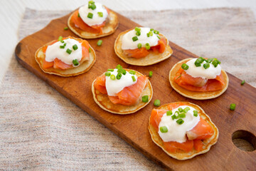 Homemade Blini with Smoked Salmon, Creme and Chives on a rustic wooden board, side view.