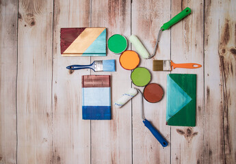 The concept of self-repair of an apartment or house. Paints and brushes are laid out on a wooden surface along with test paint strokes. Place for a copy space