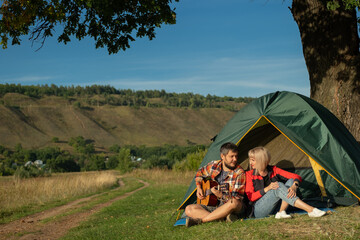 Man and woman sing a song with guitar sitting at tent. Family is on camping trip.