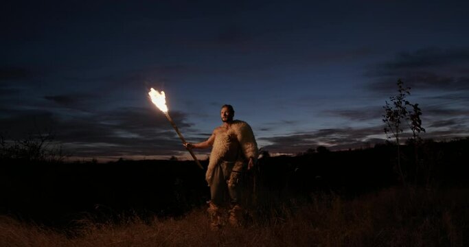Barbarian with torch exploring countryside. Low angle of man with bow and burning torch exploring wilderness against cloudy sky at night