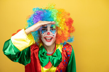 Clown standing over yellow insolated yellow background very happy and smiling looking far away with hand over head. searching concept.