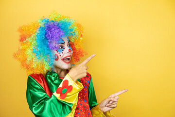 Clown standing over yellow insolated yellow background surprised and pointing her fingers side