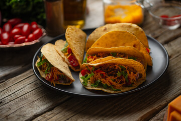 Close-up view of tasty mexican tacos on black round plate on rustic wooden table. Traditional mexican cuisine. Ingredients for cooking meal background. Concept of street food.