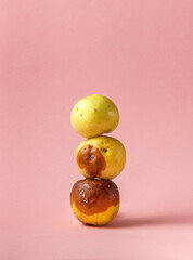 Three rotten apples stacked in a pyramid on a pink background with space. Ugly fruit, close-up.