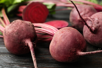 Cut and whole raw beets on wooden table, closeup